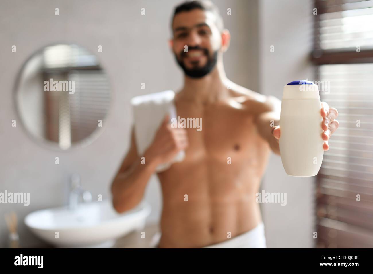 Beau jeune homme debout avec une bouteille de shampooing dans les mains Banque D'Images