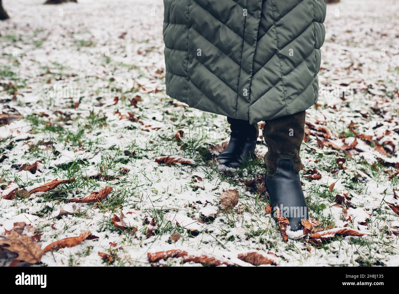 Gros plan des chaussures d'hiver pour femme.Femme marchant dans un parc enneigé avec un long manteau chaud et des bottes hautes en daim vert Banque D'Images