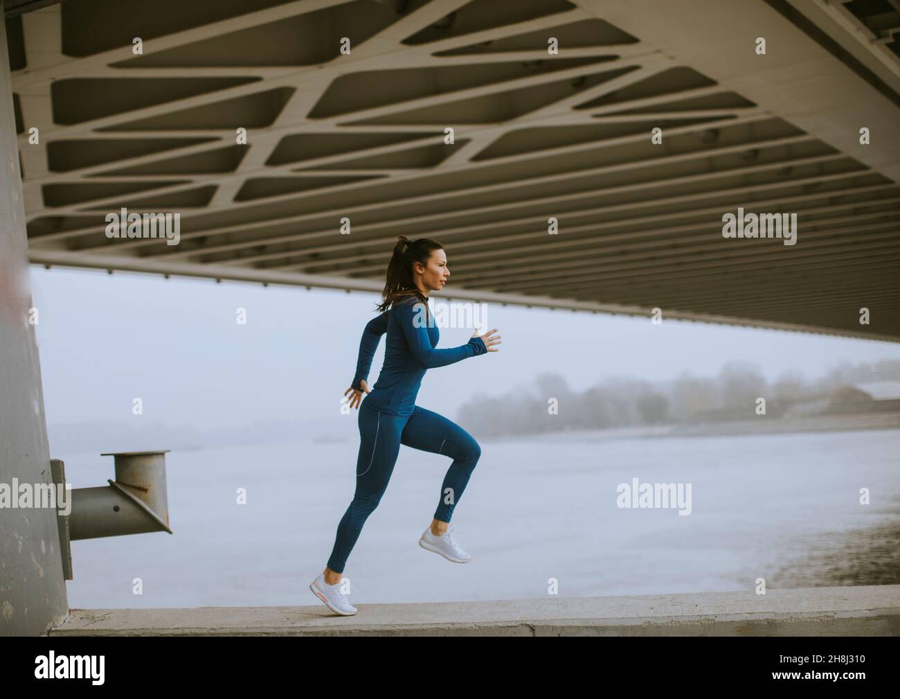 Jolie jeune femme en costume bleu sur piste qui coule au bord de la rivière à l'automne matin Banque D'Images