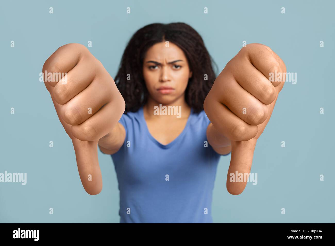 Femme noire sérieuse montrant le pouce sur fond bleu de studio Banque D'Images