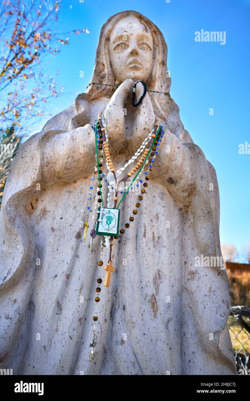 Les perles de Rosaire laissées par les visiteurs ornent une statue en pierre de la Vierge Marie au sanctuaire historique Santuario de Chimayo à Chimayo, Nouveau-Mexique, États-Unis. Banque D'Images