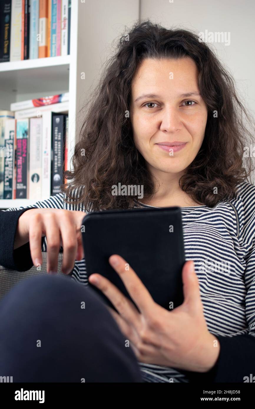 Jeune femme tenant un lecteur de livres électroniques, des livres papier en arrière-plan Banque D'Images