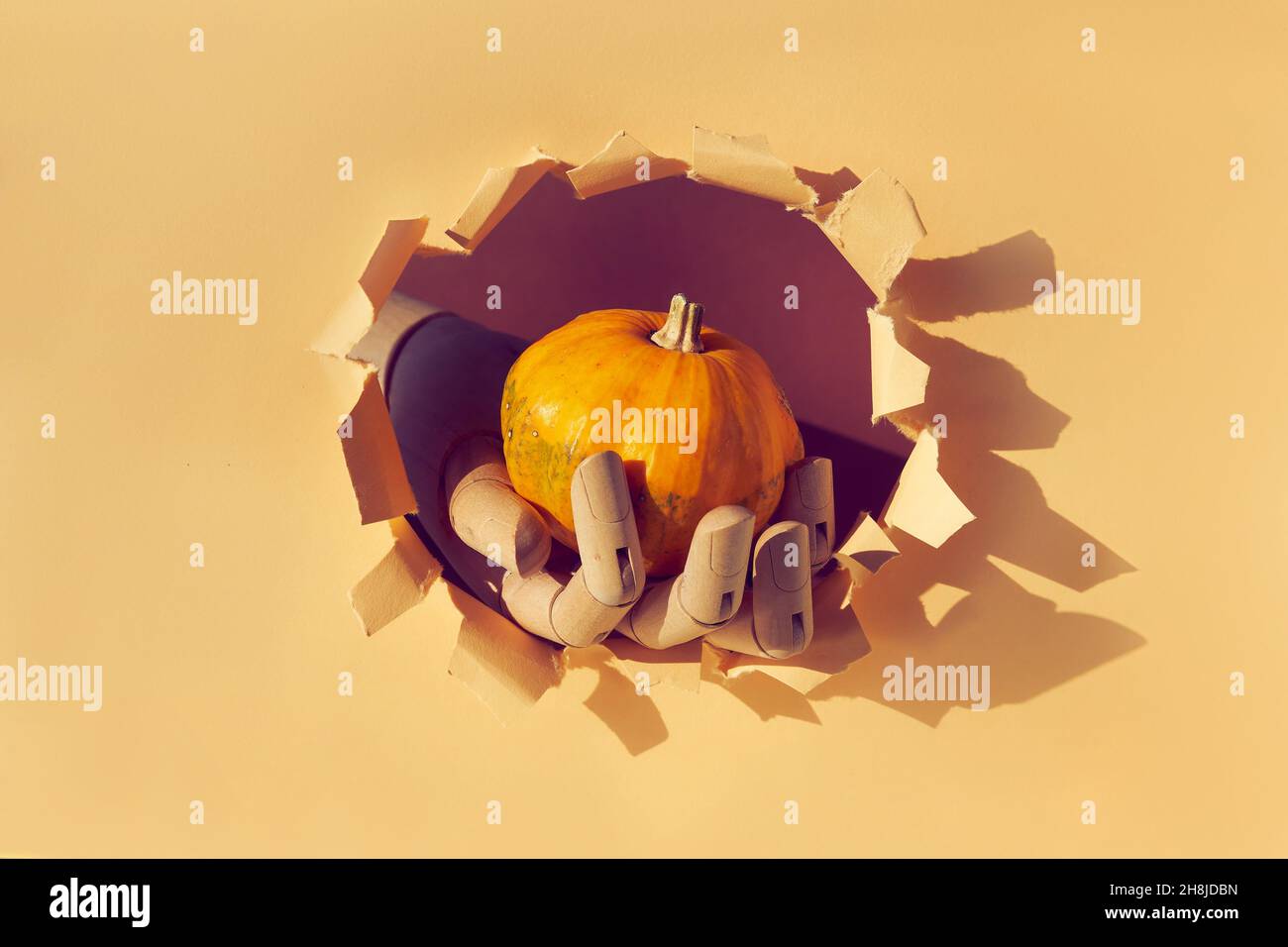 Citrouille orange en modèle de bois à travers le trou de papier dans le papier beige déchiré.Bonjour saison automne Banque D'Images