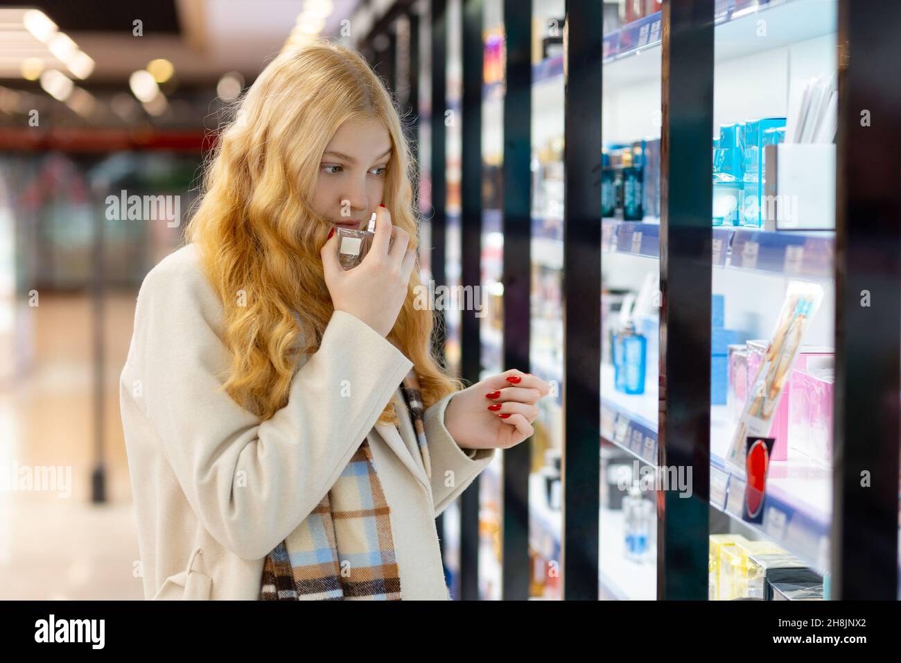 Belle jeune femme avec de longs cheveux dorés choisir le parfum dans la boutique.Recherchez un parfum pour vous-même ou comme cadeau à un être cher. Banque D'Images