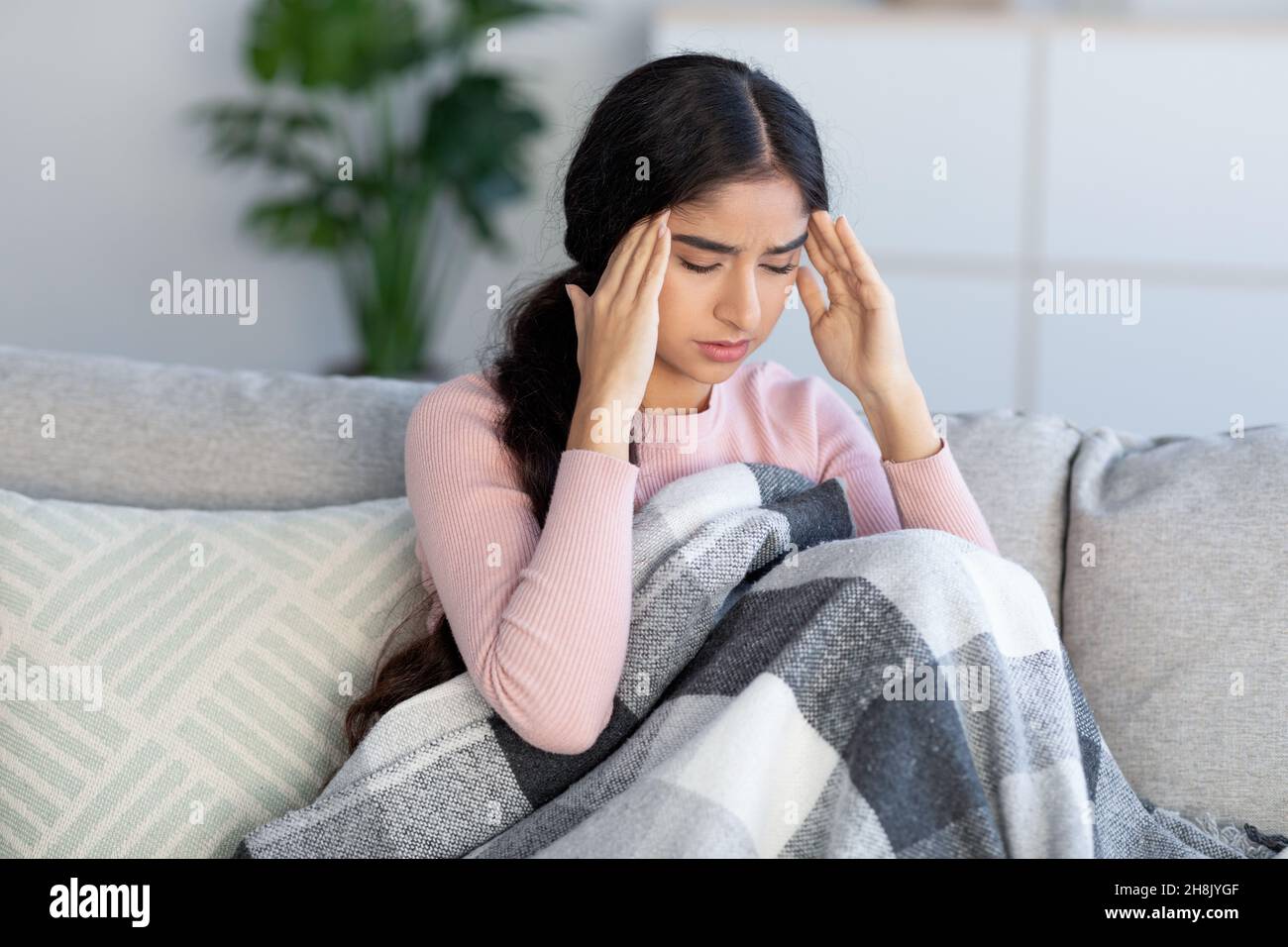Triste bouleversé jeune femme hindoue couverte de couverture, souffrant de maux de tête et de grippe, s'assoit sur le canapé et les temples de massage Banque D'Images
