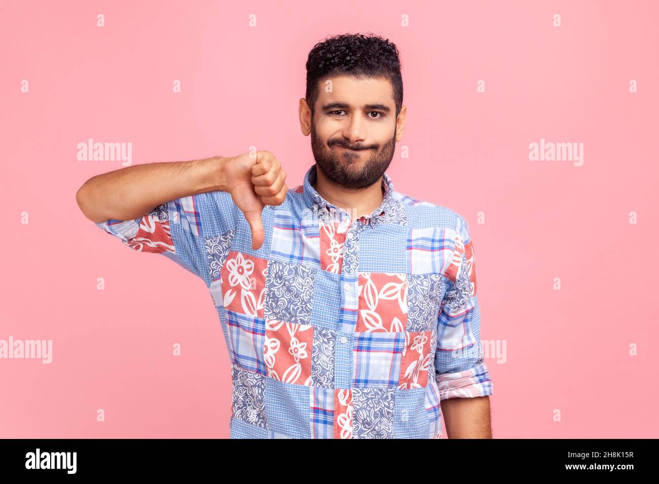 Portrait d'un jeune homme adulte en chemise bleue critiquant la mauvaise qualité avec des pouces vers le bas grimace déplaisés, montrant un geste déplaît, exprimant la désapprobation.Studio d'intérieur isolé sur fond rose. Banque D'Images