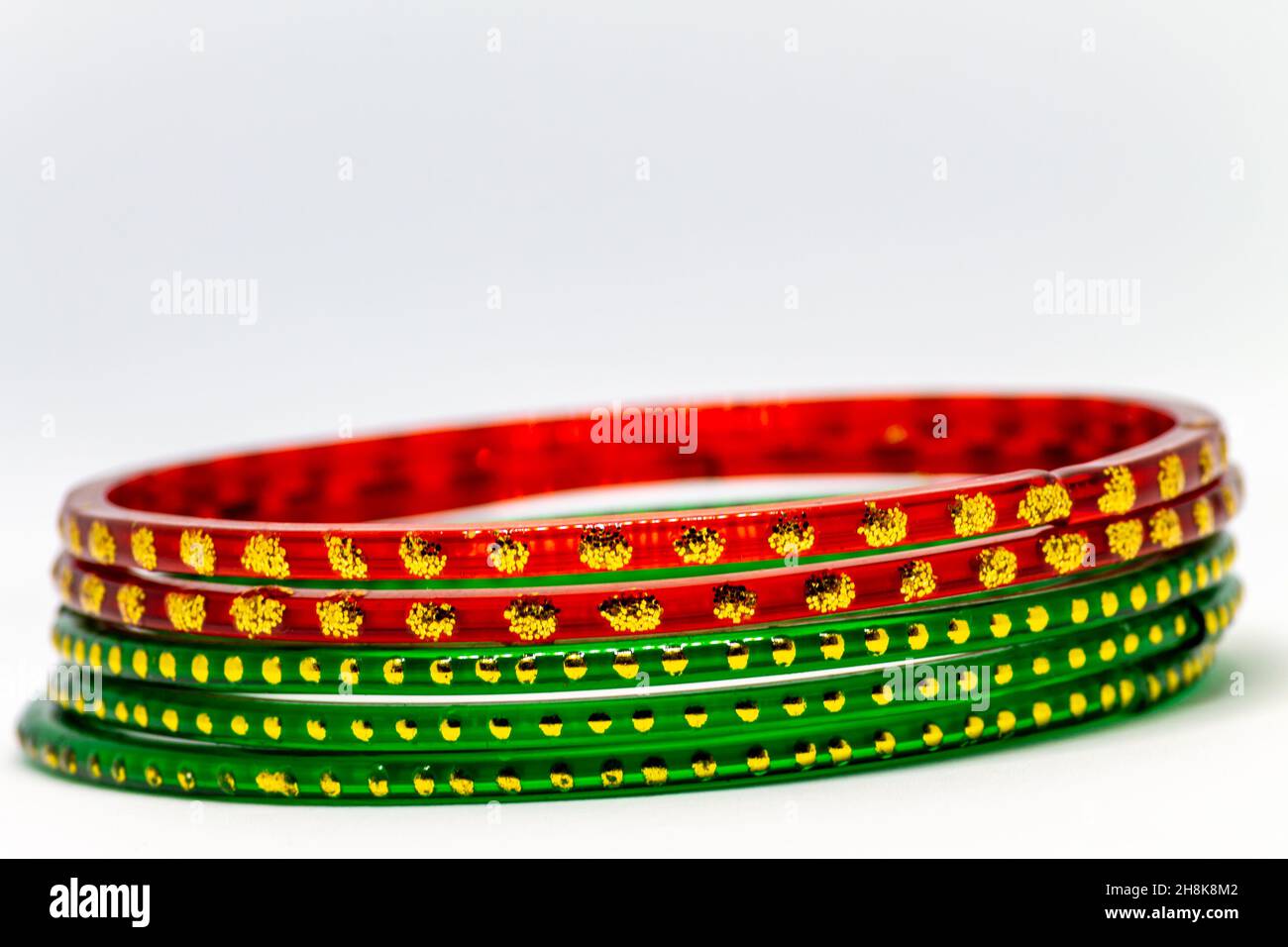 Gros plan de bracelets en verre rouge et vert (bracelets) avec des points dorés sur fond blanc Banque D'Images