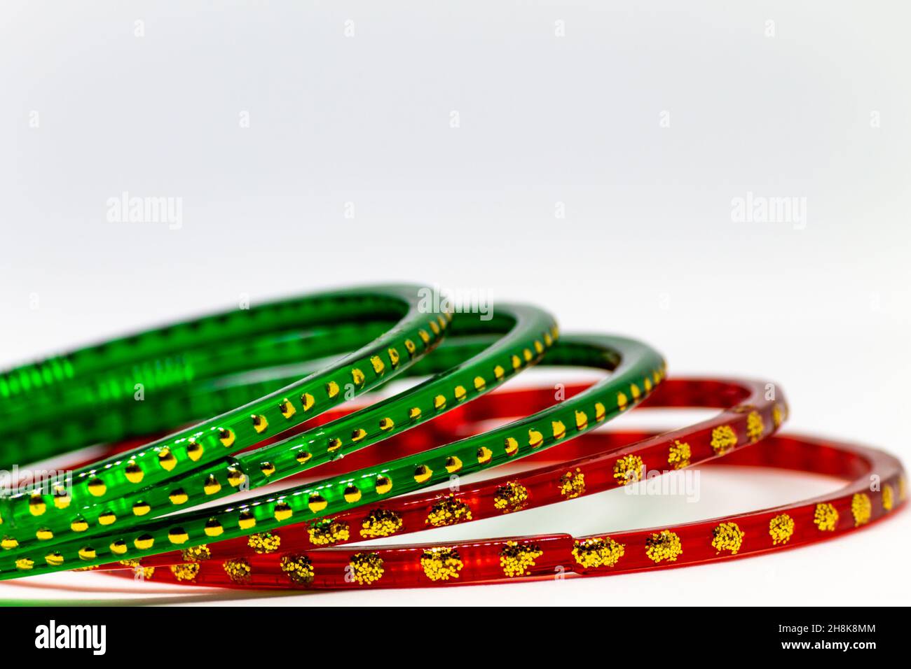 Gros plan de bracelets en verre rouge et vert (bracelets) avec des points dorés sur fond blanc Banque D'Images