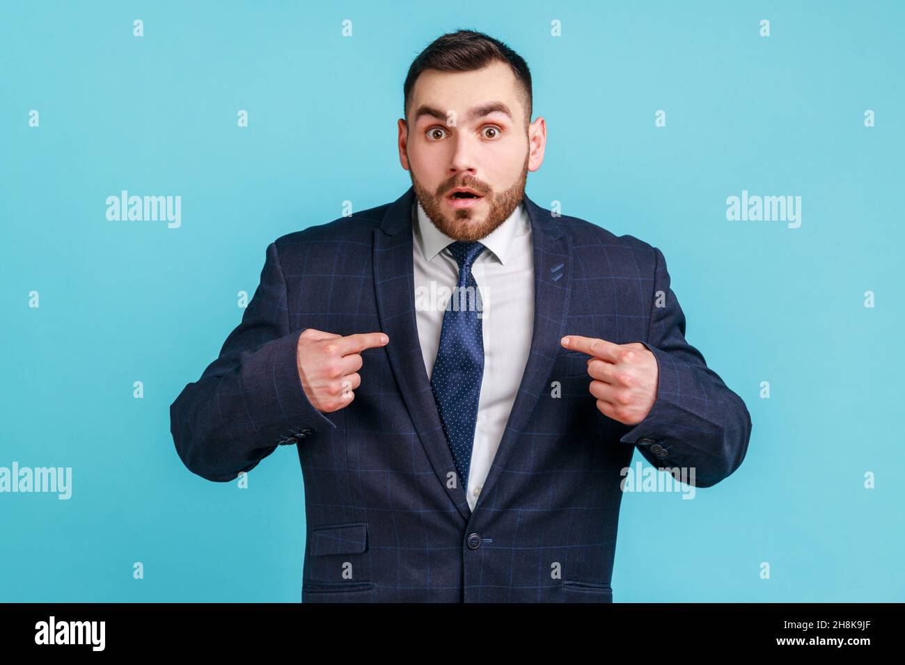 Wow, c'est moi.Portrait d'un homme d'affaires stupéfait en costume sombre, éveillant devant l'appareil photo et se pointant, choqué par son succès personnel.Studio d'intérieur isolé sur fond bleu. Banque D'Images