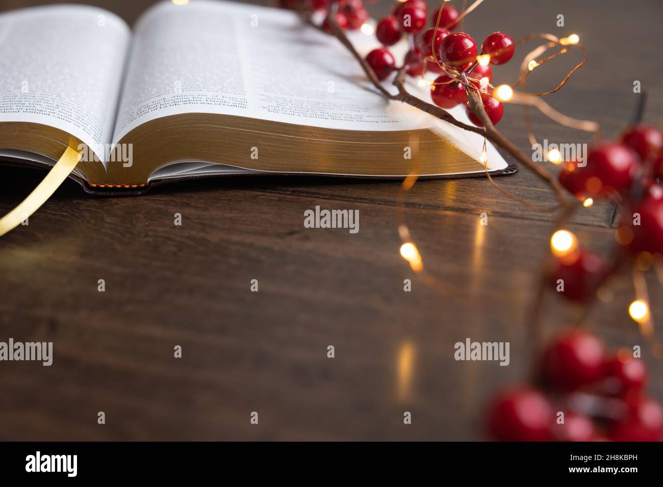 Guirlande de baies rouges et guirlande de mini-guirlandes de noël sur une bible ouverte sur un fond de bois sombre avec espace de copie Banque D'Images