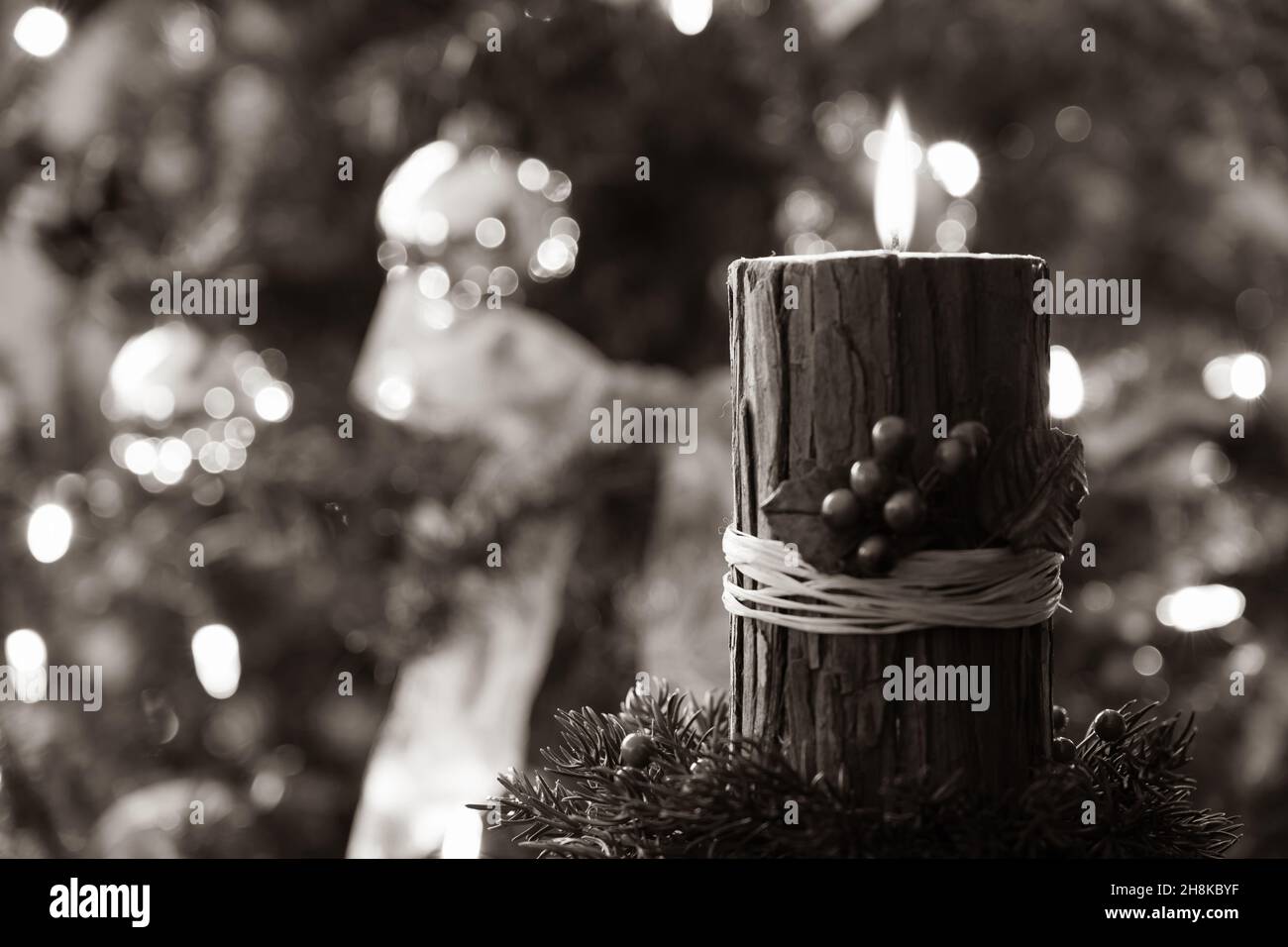 Bougie de Noël avec baies rouges et châle rustique en écorce éclairée dans une pièce sombre devant un arbre de Noël décoré Banque D'Images