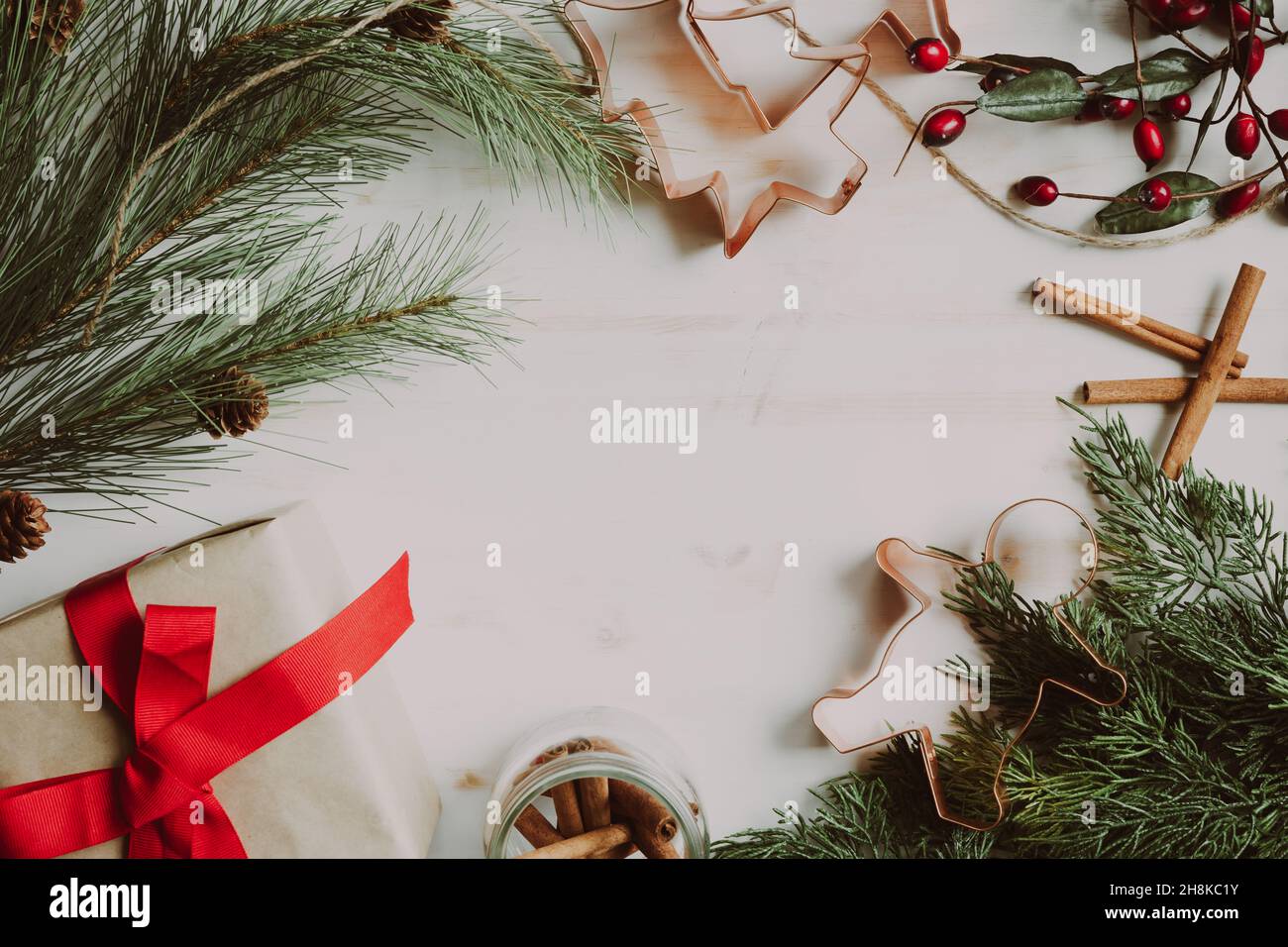 Cadre de Noël sur fond de bois blanc avec cadeau, baies rouges, creux à feuilles persistantes et emporte-pièces en cuivre Banque D'Images