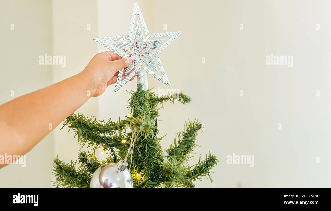 Gros plan de la main d'un garçon ou d'une fille en plaçant une étoile sur l'arbre de noël Banque D'Images