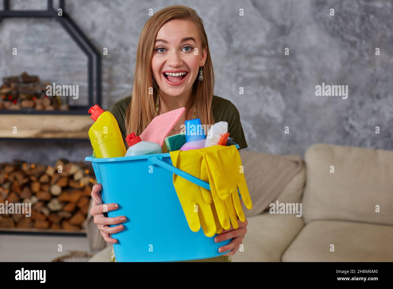Une femme de ménage est debout dans la salle de séjour, tenant un seau bleu rempli de produits chimiques et d'installations pour ranger dans sa main Banque D'Images