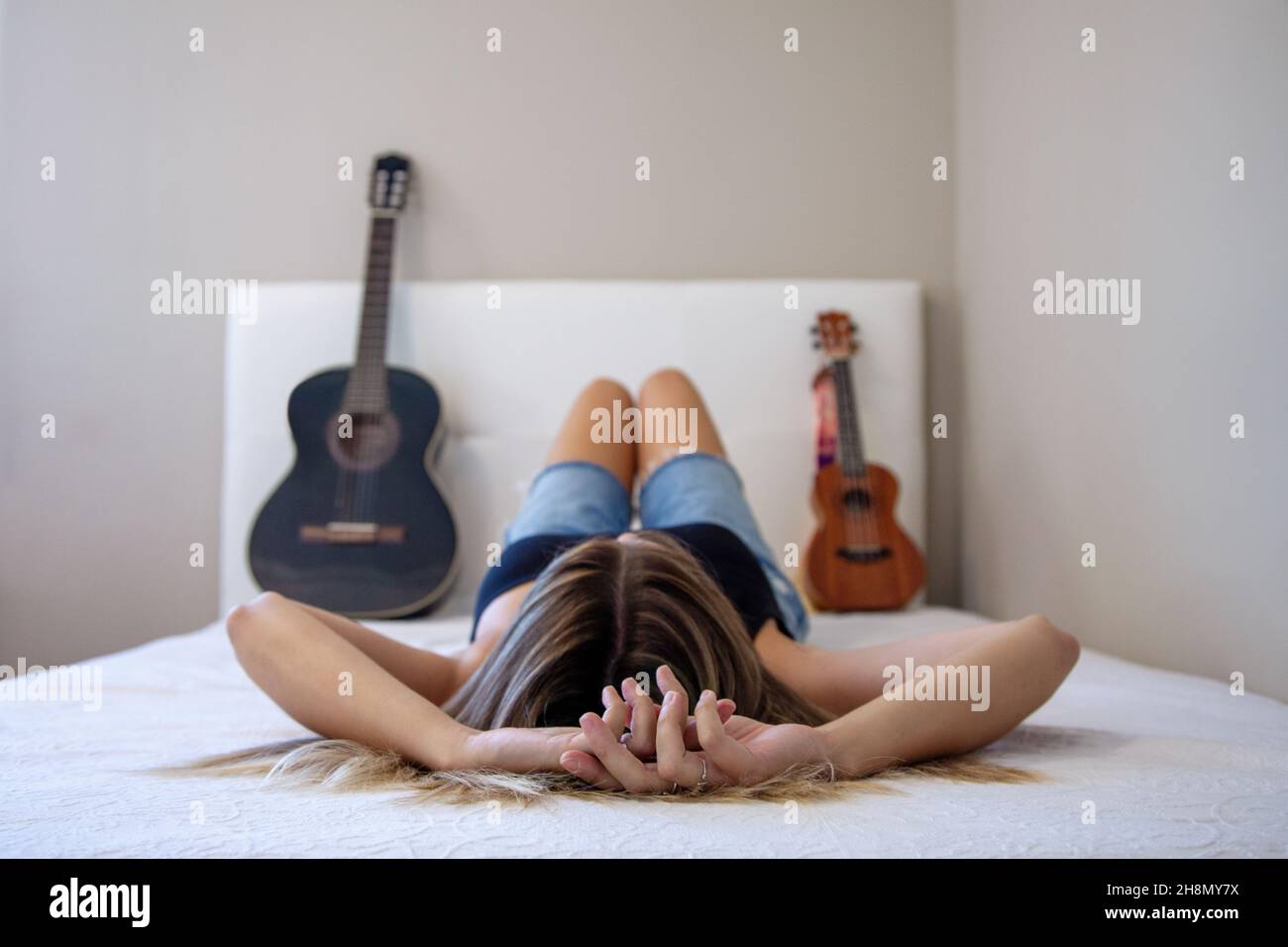 Femme avec instruments au lit. Fille avec sa guitare et son ukulele sur le lit dans sa chambre à la maison. Guitare espagnole. Banque D'Images