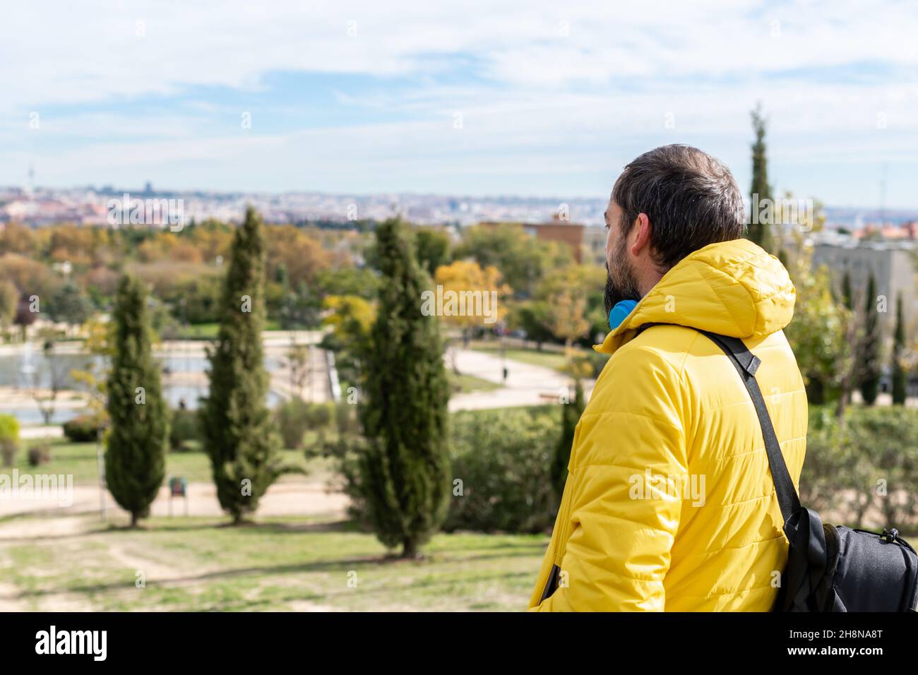 un jeune boxeur à barbe vêtu d'un manteau jaune et d'un sac à bandoulière sur le dos contemple sa ville d'un point de vue Banque D'Images
