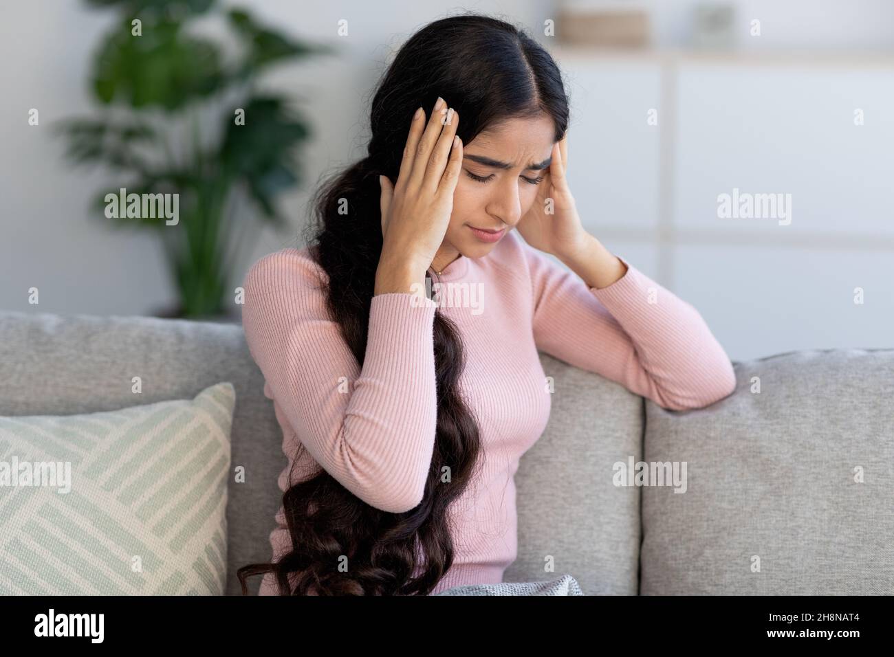 Une jeune femme hindoue contrariée et découplée souffre de maux de tête et de grippe, est assise sur un canapé et tient sa tête avec les mains Banque D'Images