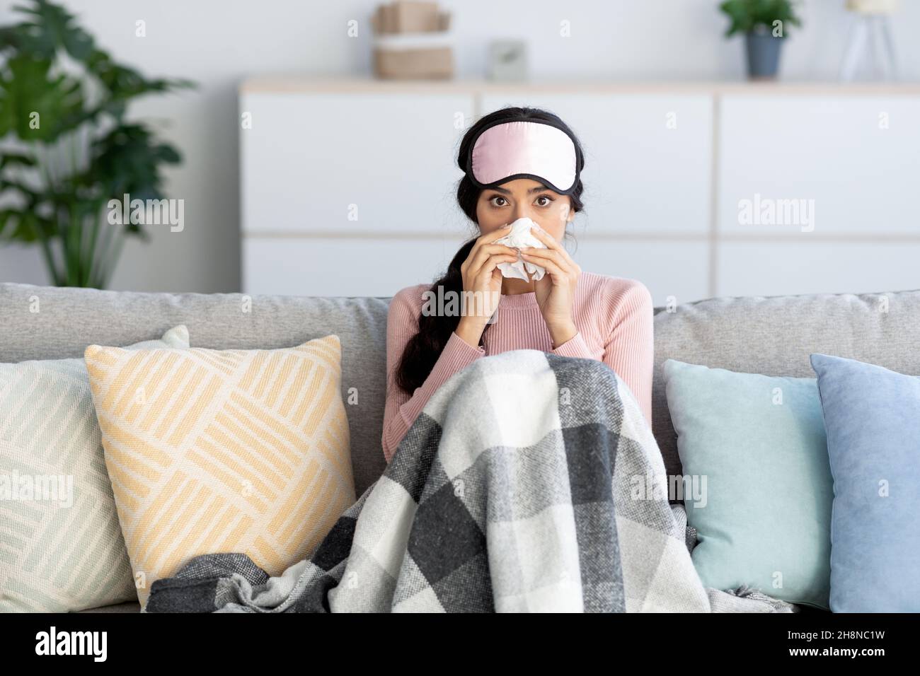 Jeune femme hindouiste dans le masque de sommeil couvert de couverture, souffre de la grippe, souffle nez dans la serviette Banque D'Images