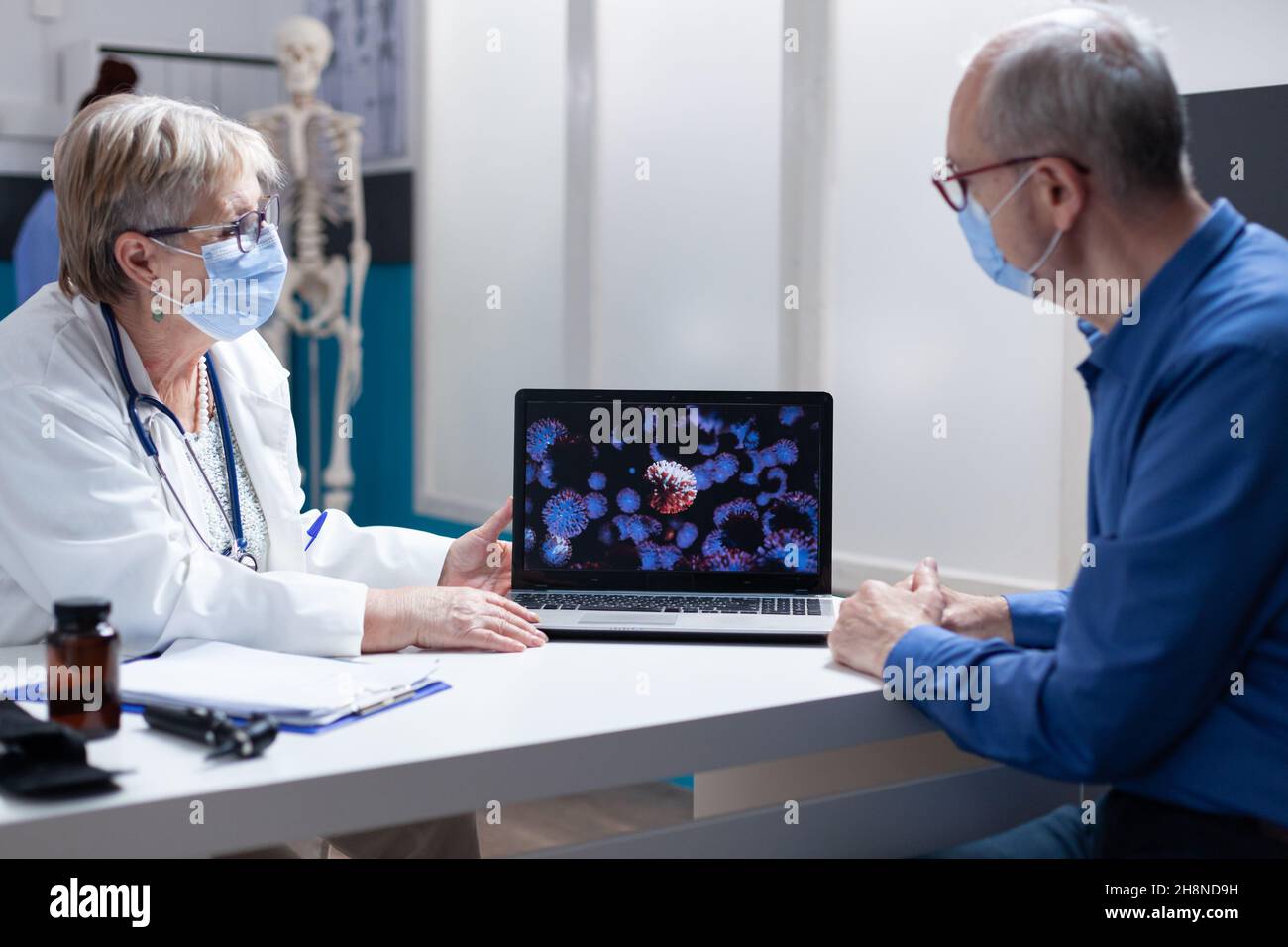 Médecin expliquant les bactéries coronavirus sur ordinateur portable à l'homme âgé, portant un masque facial dans le cabinet médical.Femme médecin montrant une représentation visuelle de la pandémie de virus lors de la visite de contrôle avec le patient Banque D'Images
