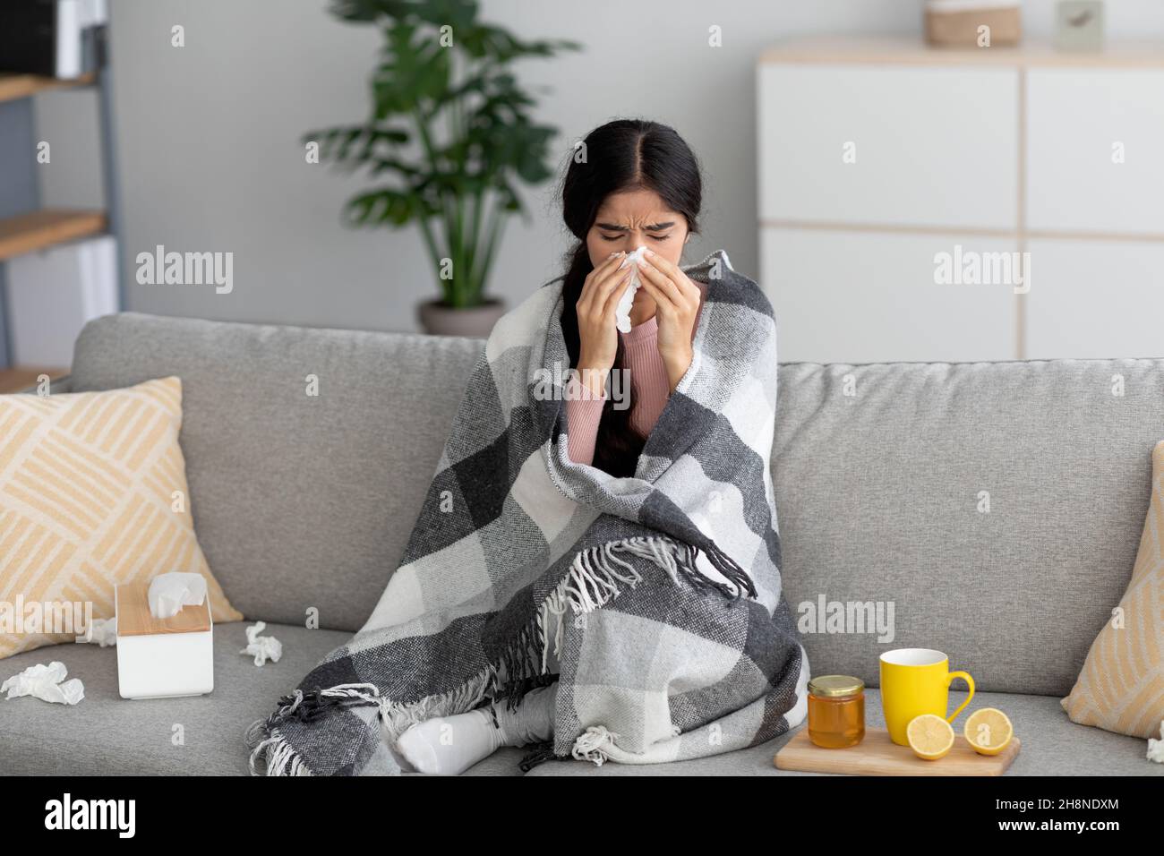 Triste femme hindoue millénaire enveloppée de plaid, souffrent de la grippe, souffle nez dans la serviette s'asseoir sur le canapé Banque D'Images