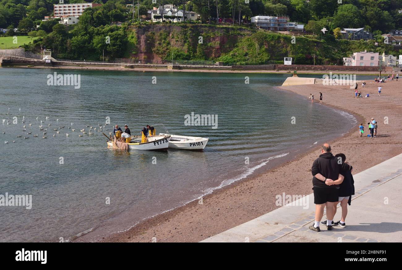 Les gens regardent les pêcheurs traînant leurs filets sur la plage de Teignmouth, dans le sud du Devon.Vue de l'autre côté de la rivière Teign vers Shaldon. Banque D'Images