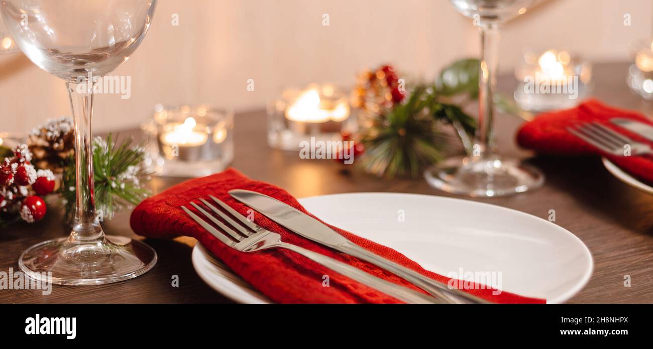 Table de Noël.Assiette et couverts sur serviette rouge.Bougies allumées sur la table la veille de Noël.Préparation d'un dîner de fête.Format de bannière Banque D'Images
