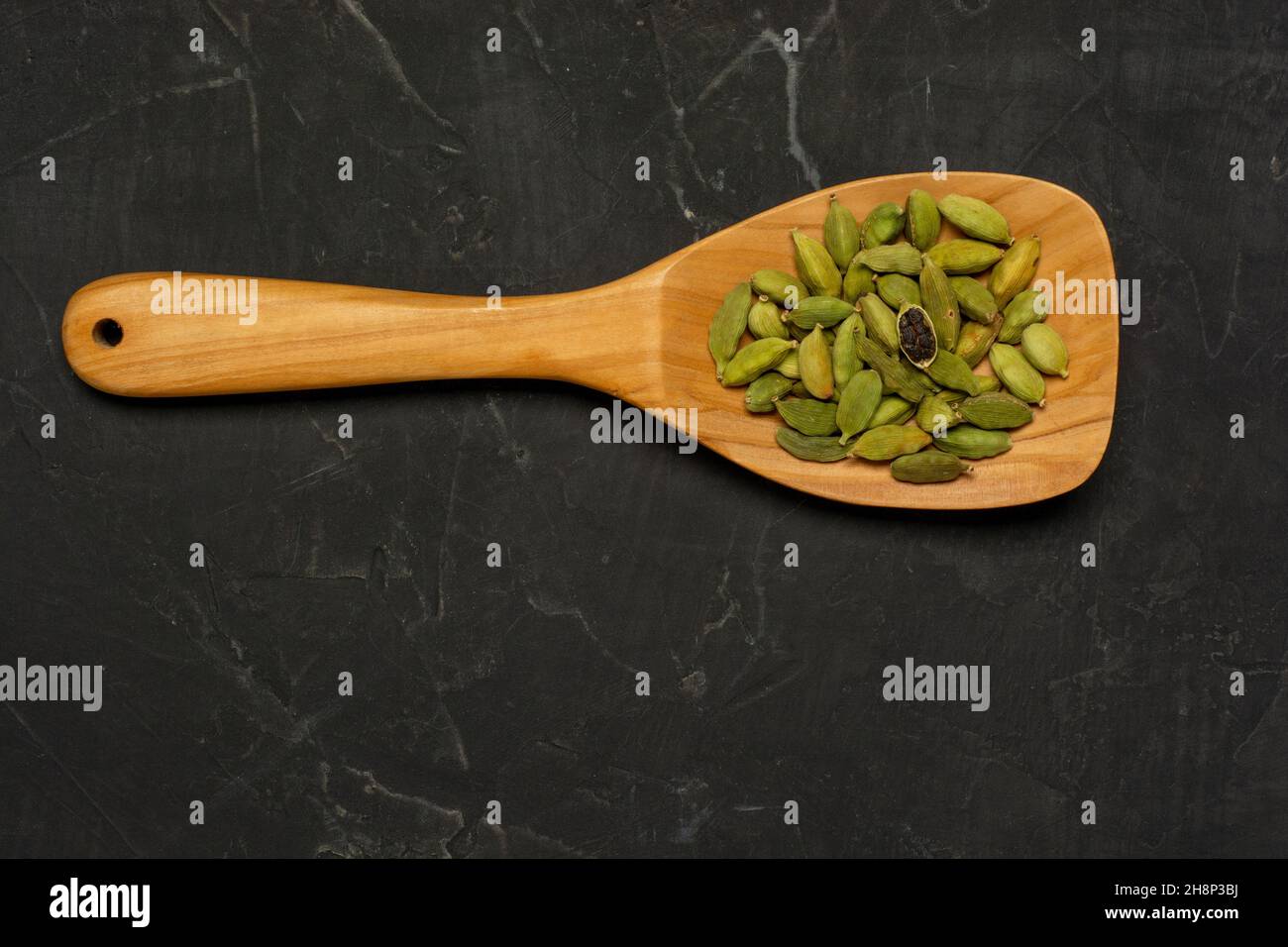 Cuillère en bois pleine de capsules de cardamome indien épicé, sur Un fond en béton foncé. Pose à plat Banque D'Images