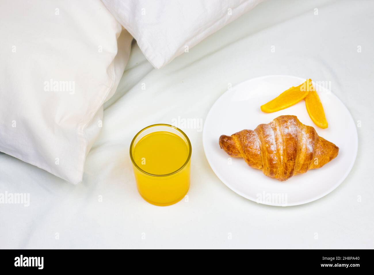 Jus d'orange frais bio et croissant sur le lit.Petit déjeuner minimum le matin au lit. Banque D'Images