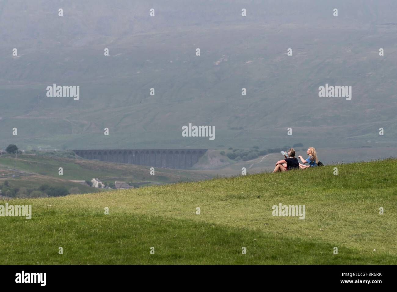 Deux randonneurs se reposant sur le sentier des trois pics se sont fortement concentrés sur un foyer doux, toile de fond brumeuse de la colline de Whernside et du viaduc de Ribblehead. Banque D'Images