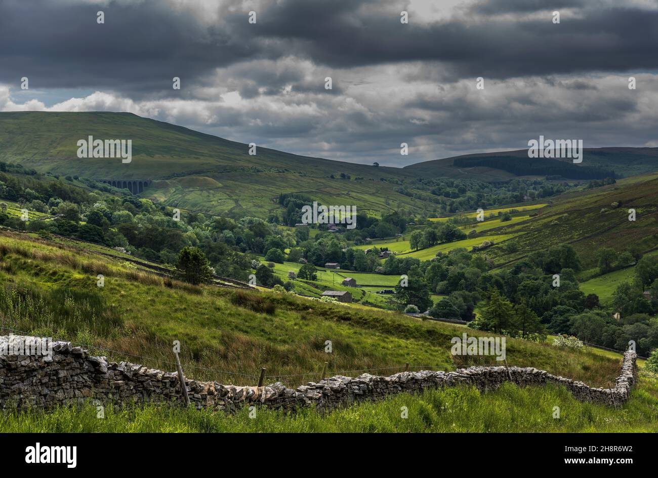 Vue sur Dentdale avec mur et pâturage traditionnels en pierre sèche en premier plan; champs, bâtiments de ferme en pierre et chemin de fer Settle-Carlisle en arrière-plan. Banque D'Images