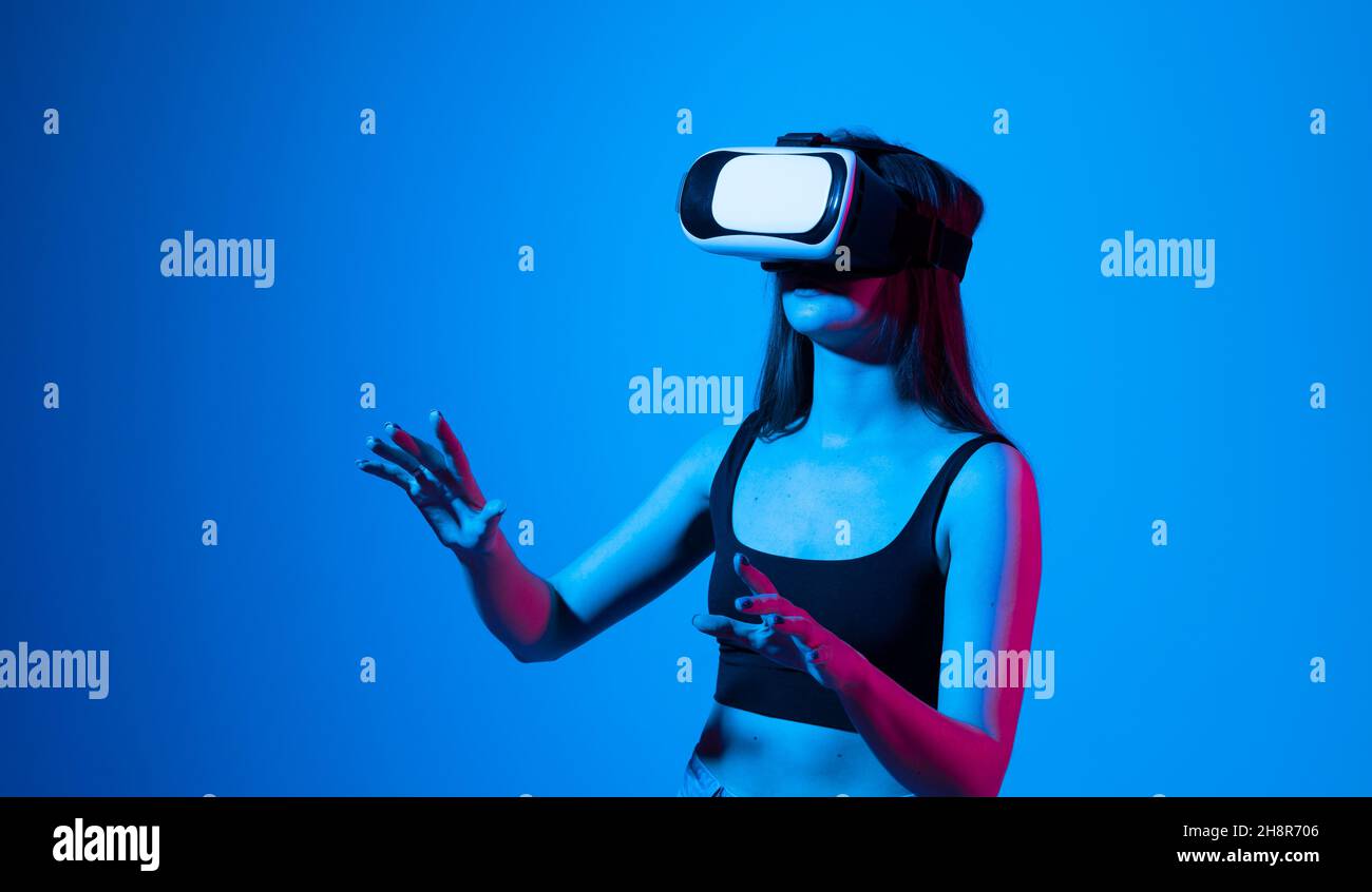 Femme avec des lunettes de réalité virtuelle dans une lumière de néon.Concept technologique futur.Une jeune femme touche l'air tout en portant des lunettes VR. Banque D'Images