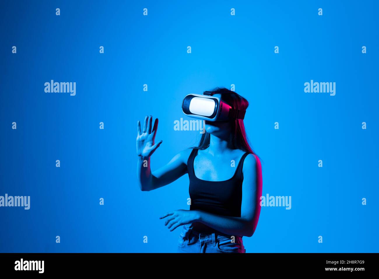 Gros plan d'une jeune femme se tient en studio avec des lunettes VR et fait glisser les mains pour zoomer en faisant défiler dans un espace virtuel tout en interagissant avec un objet Banque D'Images