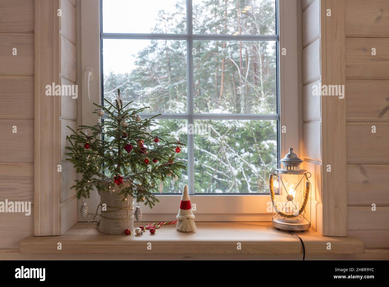 Lanterne de Noël, gnome de Noël, sapin de Noël et décoration rouge sur la fenêtre d'une maison en bois Banque D'Images