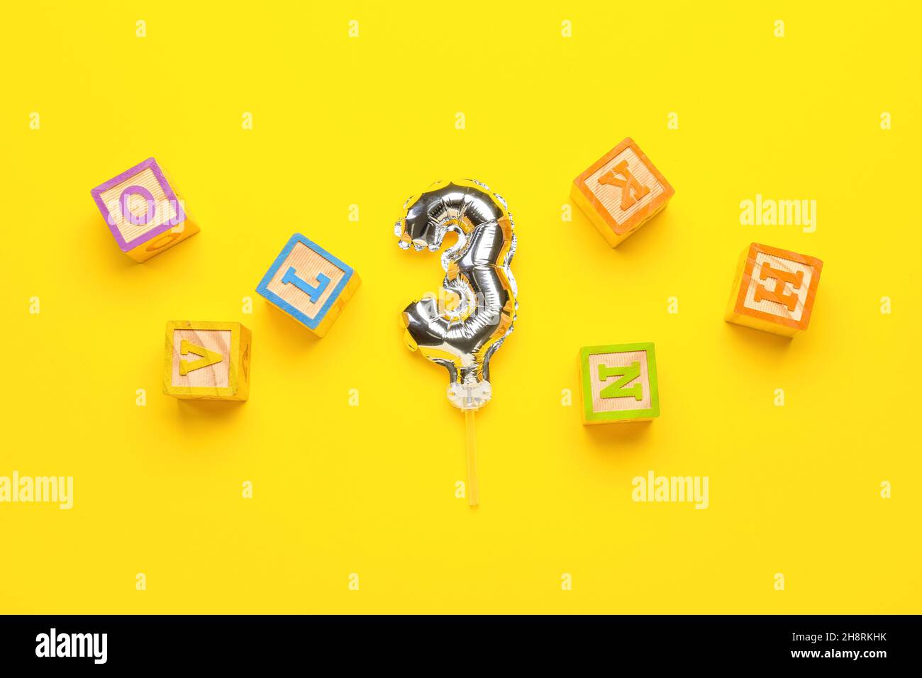 Ballon d'argent en forme de figure 3 et cubes en bois avec des lettres sur fond jaune Banque D'Images