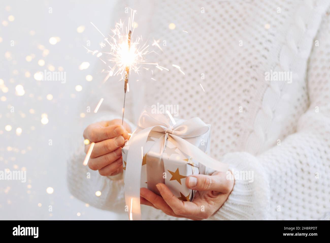 Une fille dans un chandail blanc tient un cadeau et des Sparklers étincelants.Concept de vacances nouvel an ou Noël.Mise au point sélective Banque D'Images