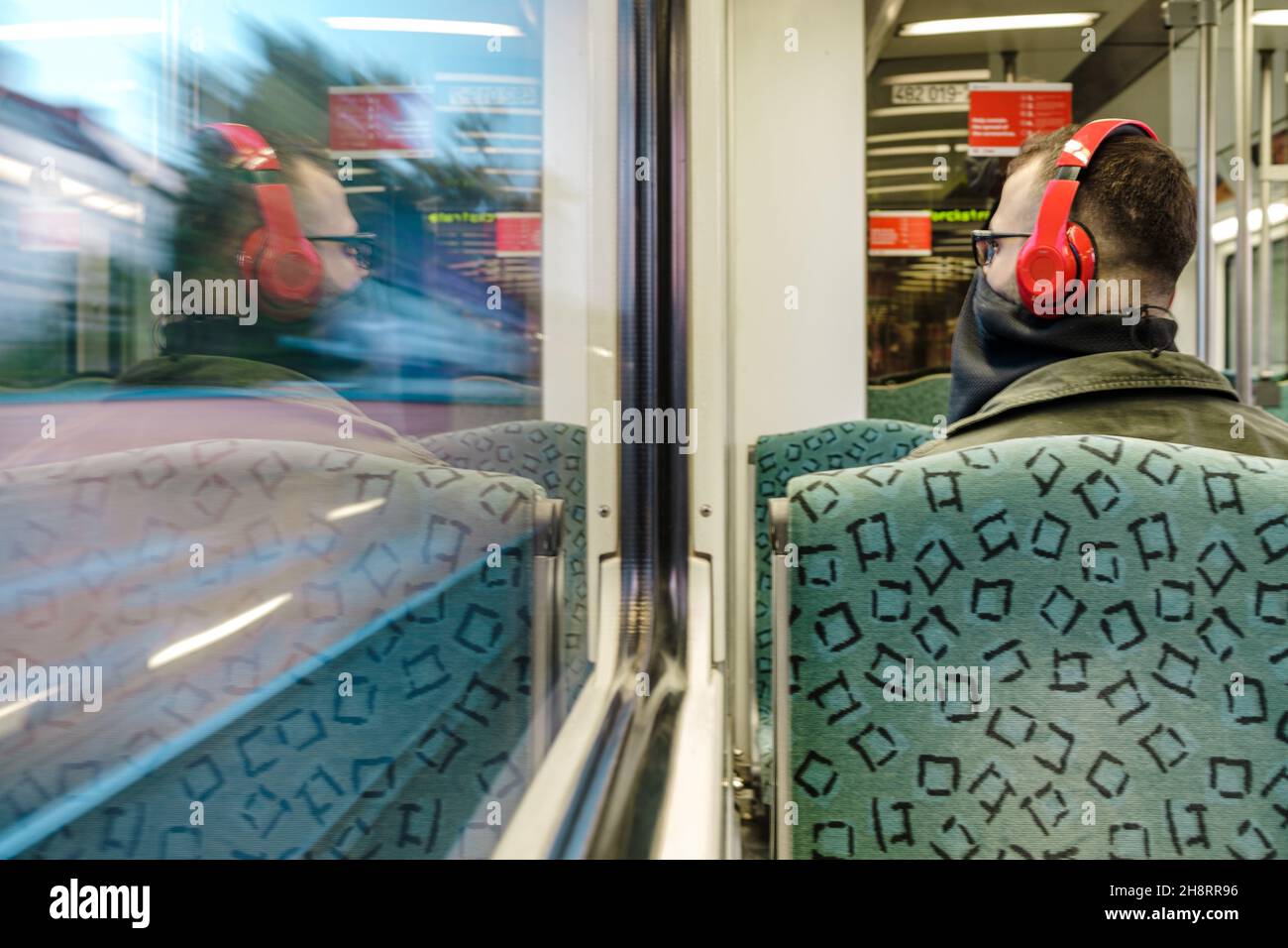BERLIN, ALLEMAGNE - 23 mai 2020 : un jeune homme dans le train Sbahn Berlin écoute de la musique avec son casque rouge et porte un masque Banque D'Images