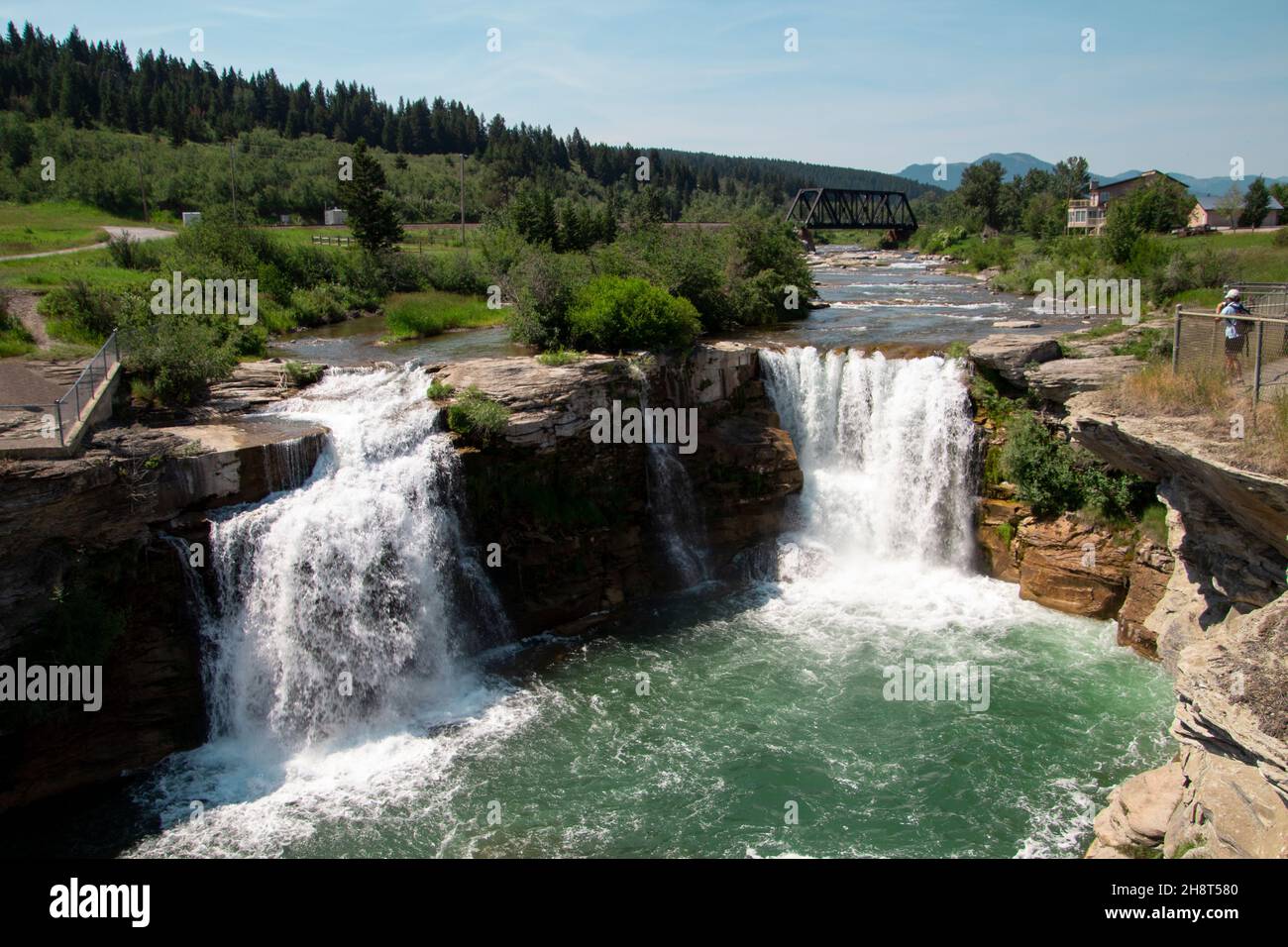 Vue sur le paysage en descendant sur les doubles chutes d'eau de Lundbreck avec rivière, pont et petites montagnes en arrière-plan. Ciel bleu arbres verts Banque D'Images