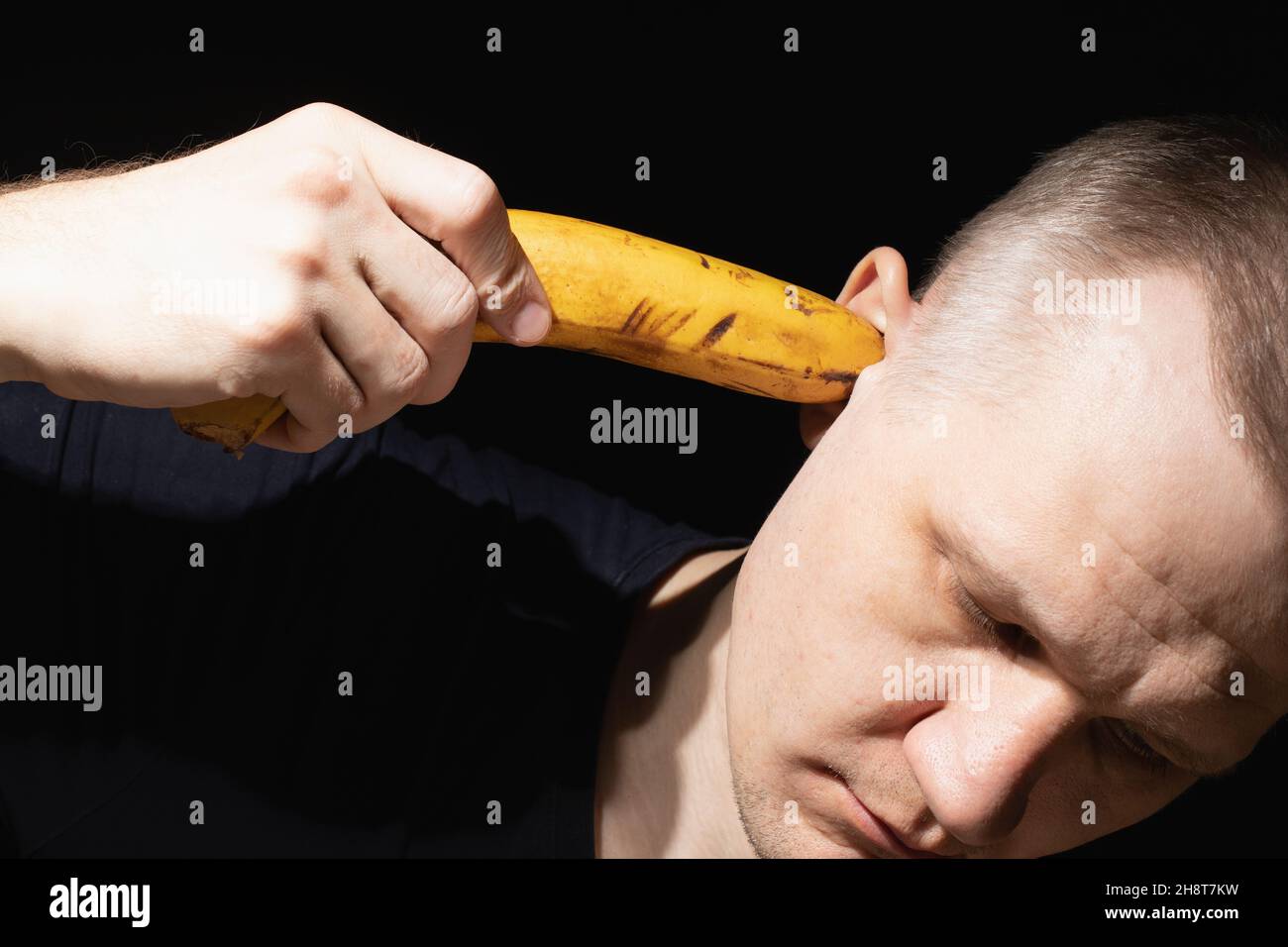 Homme tient la banane dans son oreille gros plan sur fond noir.Concept de l'incapacité à comprendre les autres et de la surdité envers le reste du monde.Relations humaines Banque D'Images