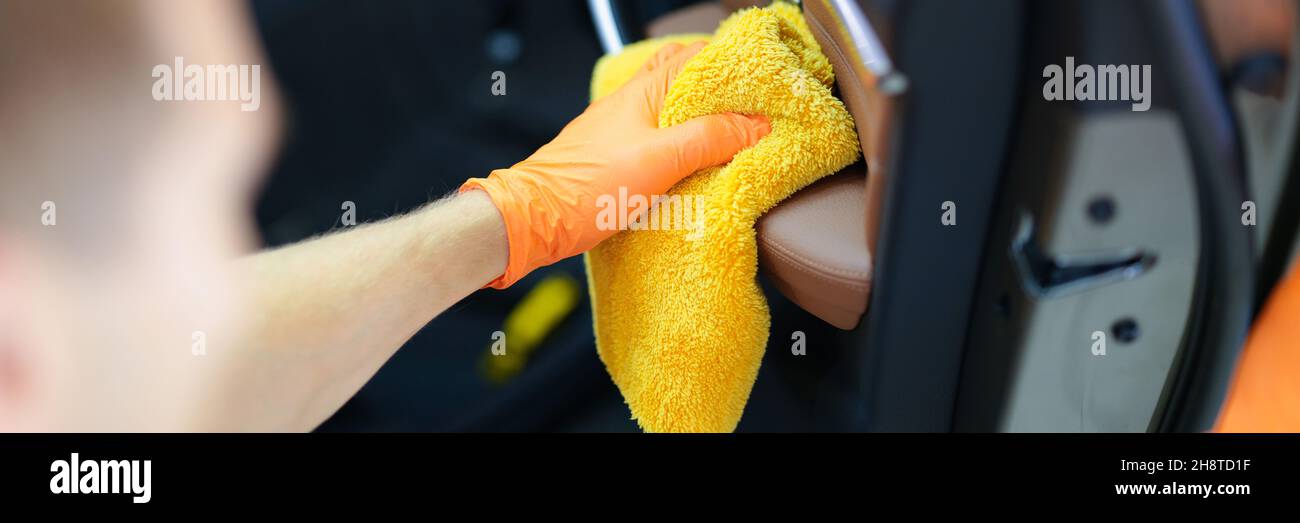 Homme dans des gants en caoutchouc essuyant la poussière de la porte de voiture avec un chiffon en microfibre Banque D'Images