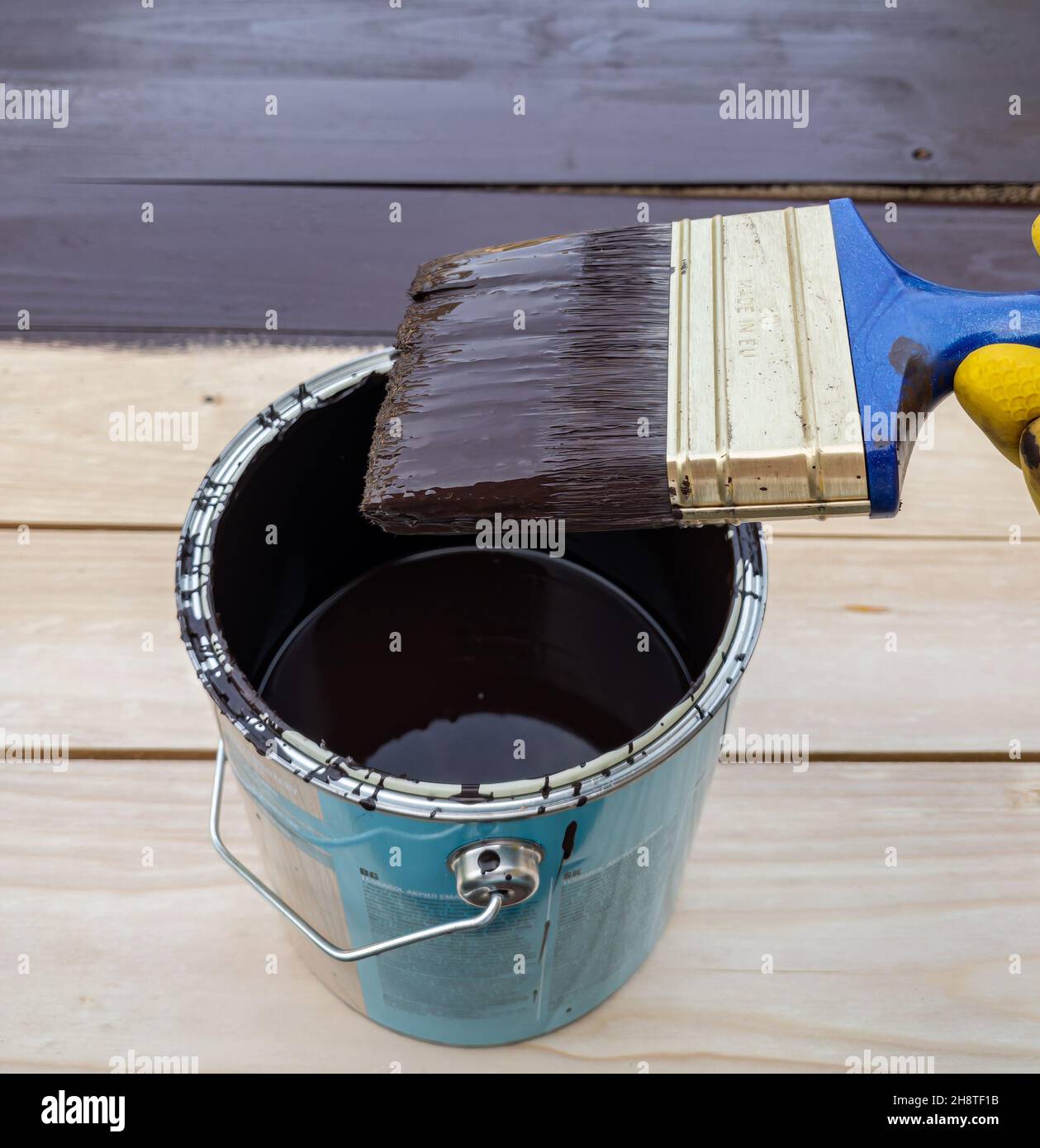 Ljubljana, Slovénie - 24 juillet 2021 : une main dans des gants jaunes, tenant une brosse de couleur marron, avec des planches peintes en arrière-plan Banque D'Images