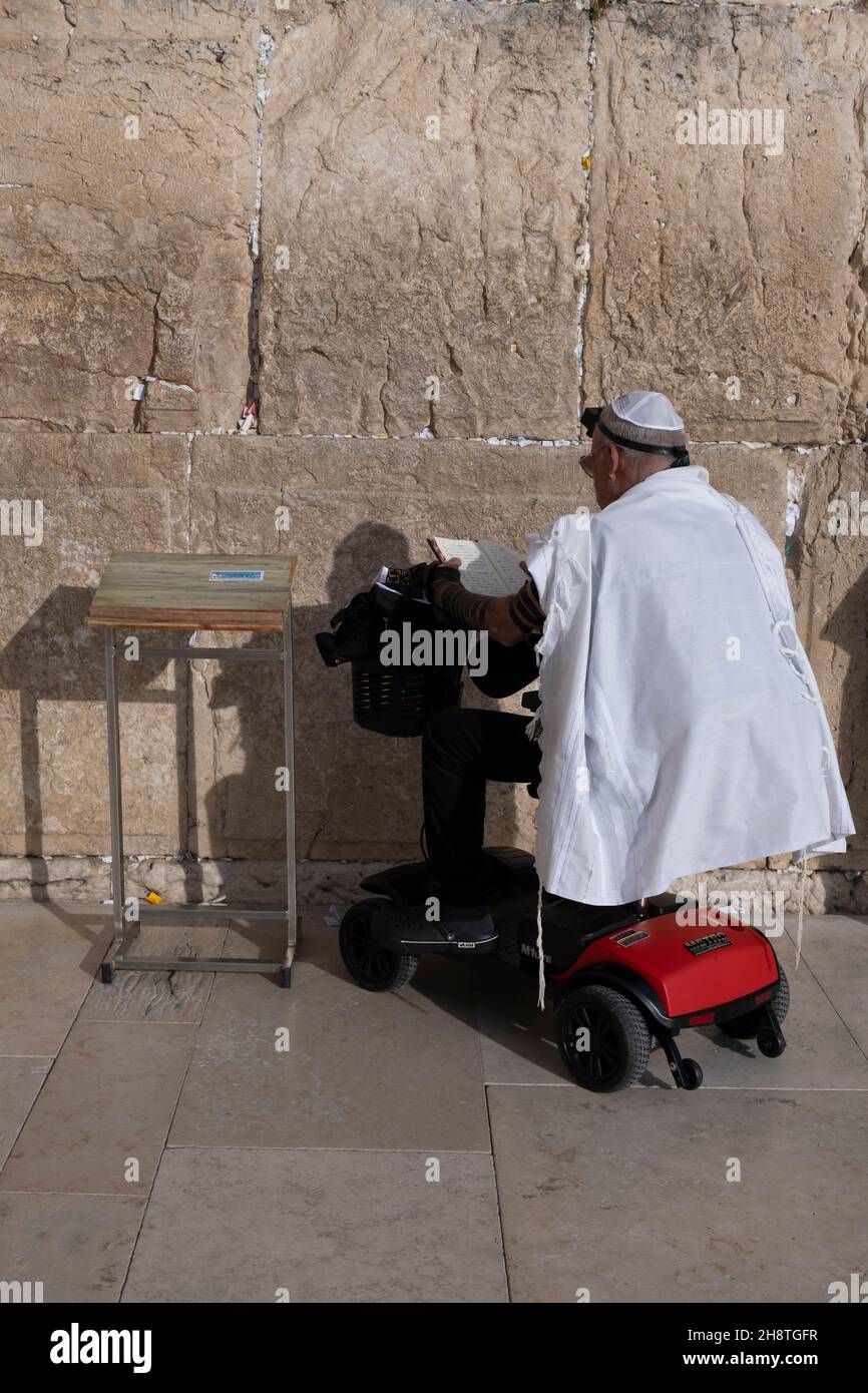 Un juif religieux enveloppé de Tait Shawl traditionnel et de Tylcaractéristiques de Tefillin prie alors qu'il est assis sur un fauteuil roulant motorisé au mur occidental ou à la vieille ville de Kotel Jérusalem-est Israël Banque D'Images