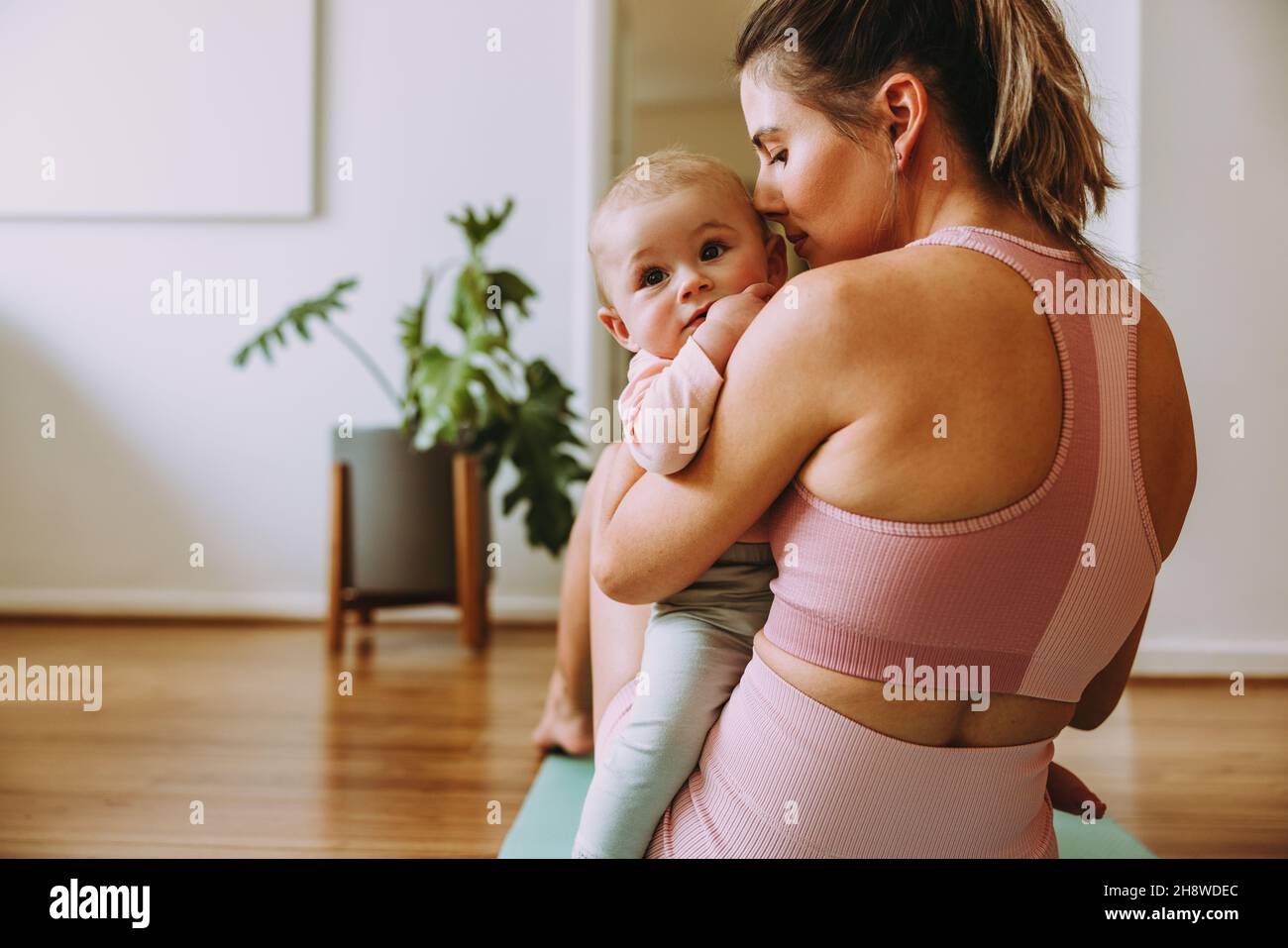 Maman qui s'occupe de l'activité avec son bébé à la maison.Maman aimante tenant son bébé tout en étant assise sur un tapis d'exercice.Une nouvelle maman se liant à son bébé pendant son p Banque D'Images