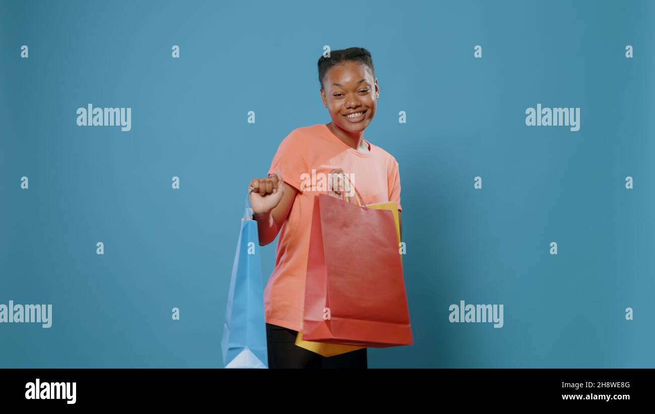 Une femme joyeuse dansant et tenant des sacs de shopping après avoir fait le paiement dans un magasin de détail.Bonne personne achetant des vêtements dans des sacs de papier colorés et montrant l'achat devant l'appareil photo. Banque D'Images