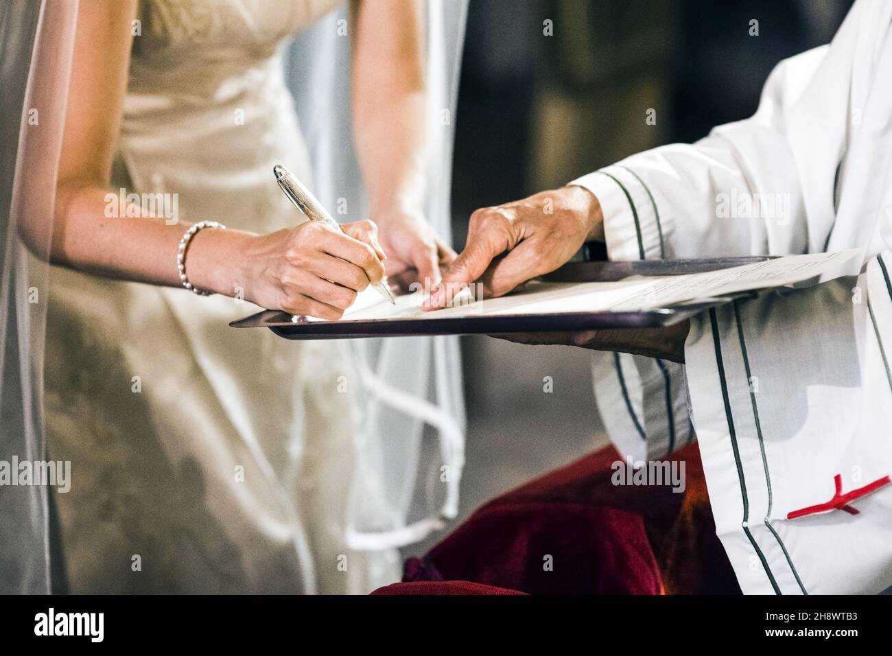 Une mariée signe son contrat de mariage sur l'autel d'une église avec un prêtre. Banque D'Images