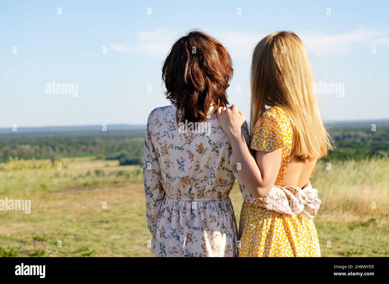 Deux modèles caucasiens féminins en robes embrassent l'extérieur ensoleillé jour, vue arrière.Amitié ou romance concept Banque D'Images