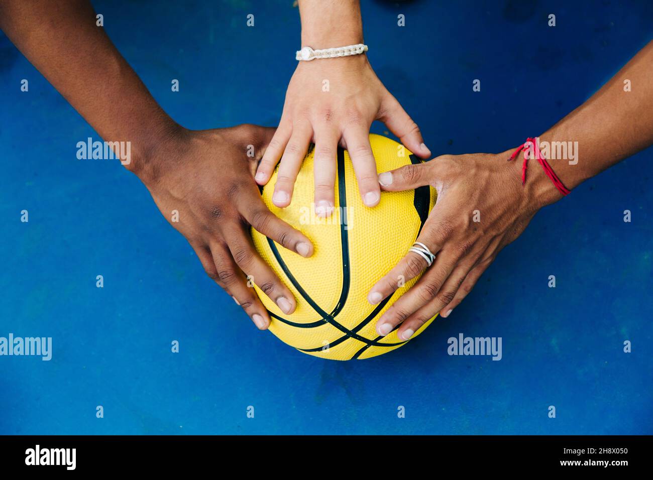 De dessus de crop anonyme joueurs masculins mettant les mains sur le ballon jaune de basket-ball sur la surface bleue de sportsground Banque D'Images