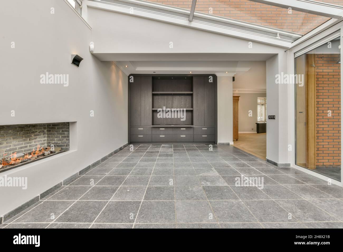 Pile de bois de chauffage brûlant dans une cheminée moderne en brique au mur blanc sur la salle lumineuse avec sol carrelé dans l'appartement Banque D'Images