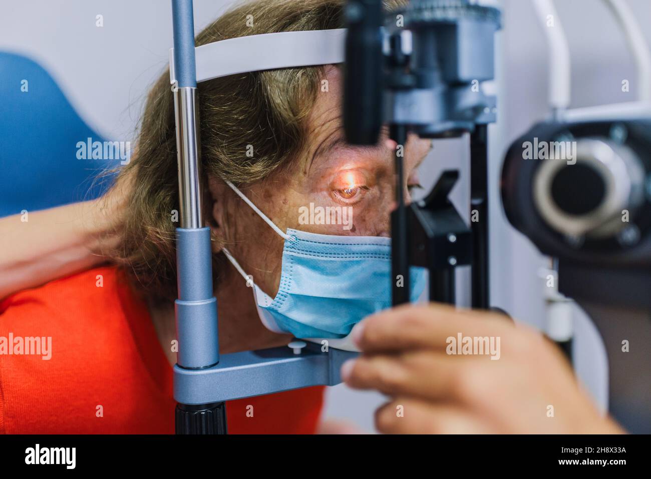 Adulte médecin ophtalmologiste dans le masque de protection vérifiant la vue de la patiente senior avec l'ophtalmoscope Banque D'Images