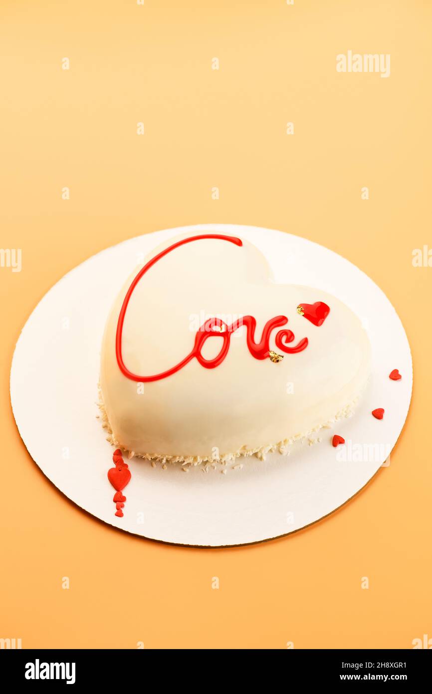 Mousse le gâteau en forme de coeur avec l'inscription Love sur fond orange pour la Saint-Valentin et le 14 février Banque D'Images