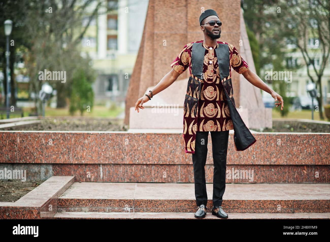 Homme africain élégant et beau dans une tenue traditionnelle, lunettes de  soleil et casquette noire debout à l'extérieur contre monument Photo Stock  - Alamy